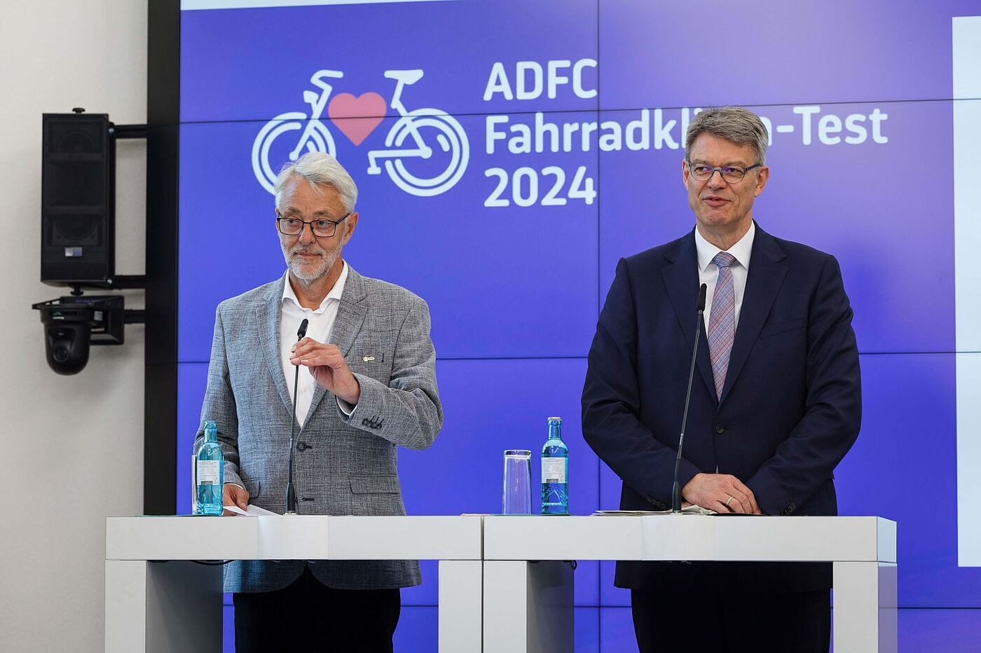 Zwei Männer stehen an Rednerpulten vor einer Präsentationsfläche mit dem Logo des ADFC Fahrradklima-Tests 2024.