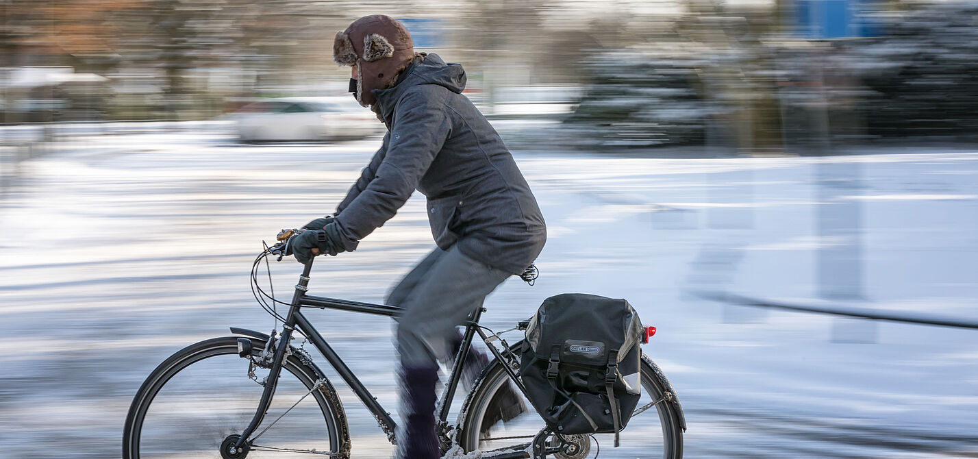 Mann fährt auf ungeräumten Radweg im Winter